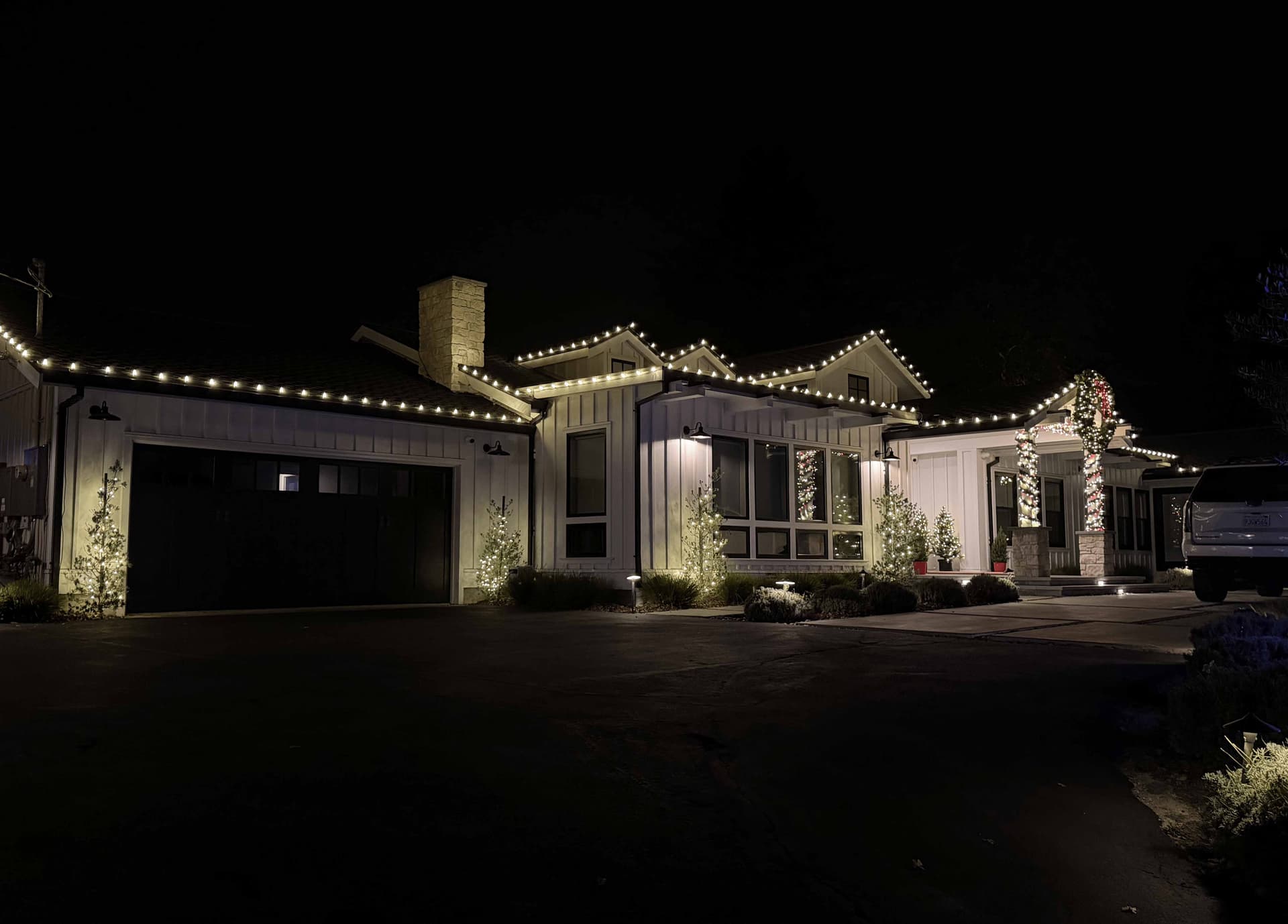 Two-story home with full roofline Christmas lighting and lit topiaries at night
