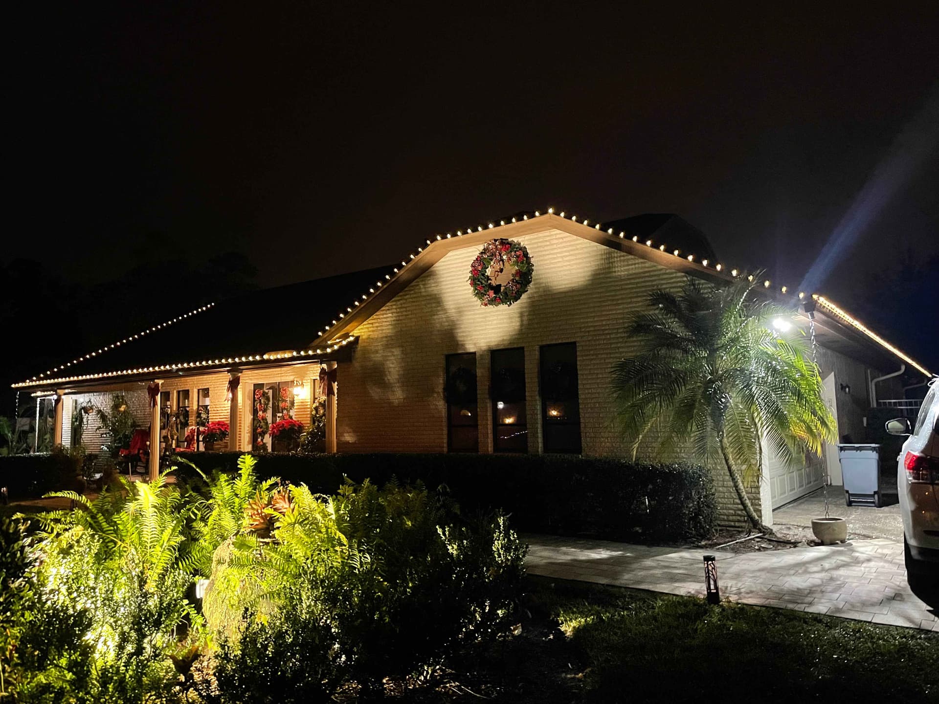 Warm-white C9 roofline on a single-story brick ranch home with wreath and landscape uplighting