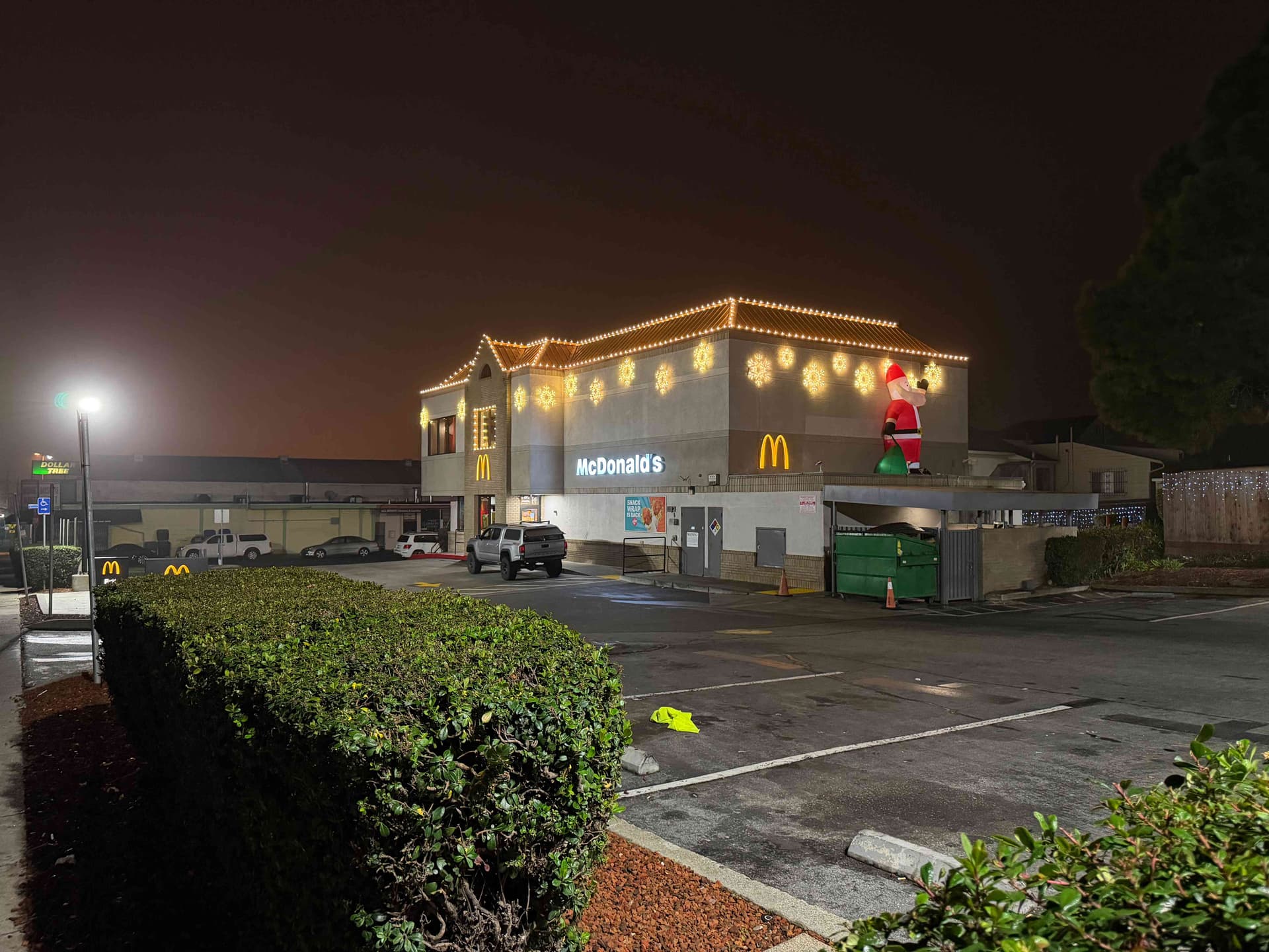 Two-story McDonald's with warm white C9 roofline, snowflake motifs, and a rooftop inflatable Santa