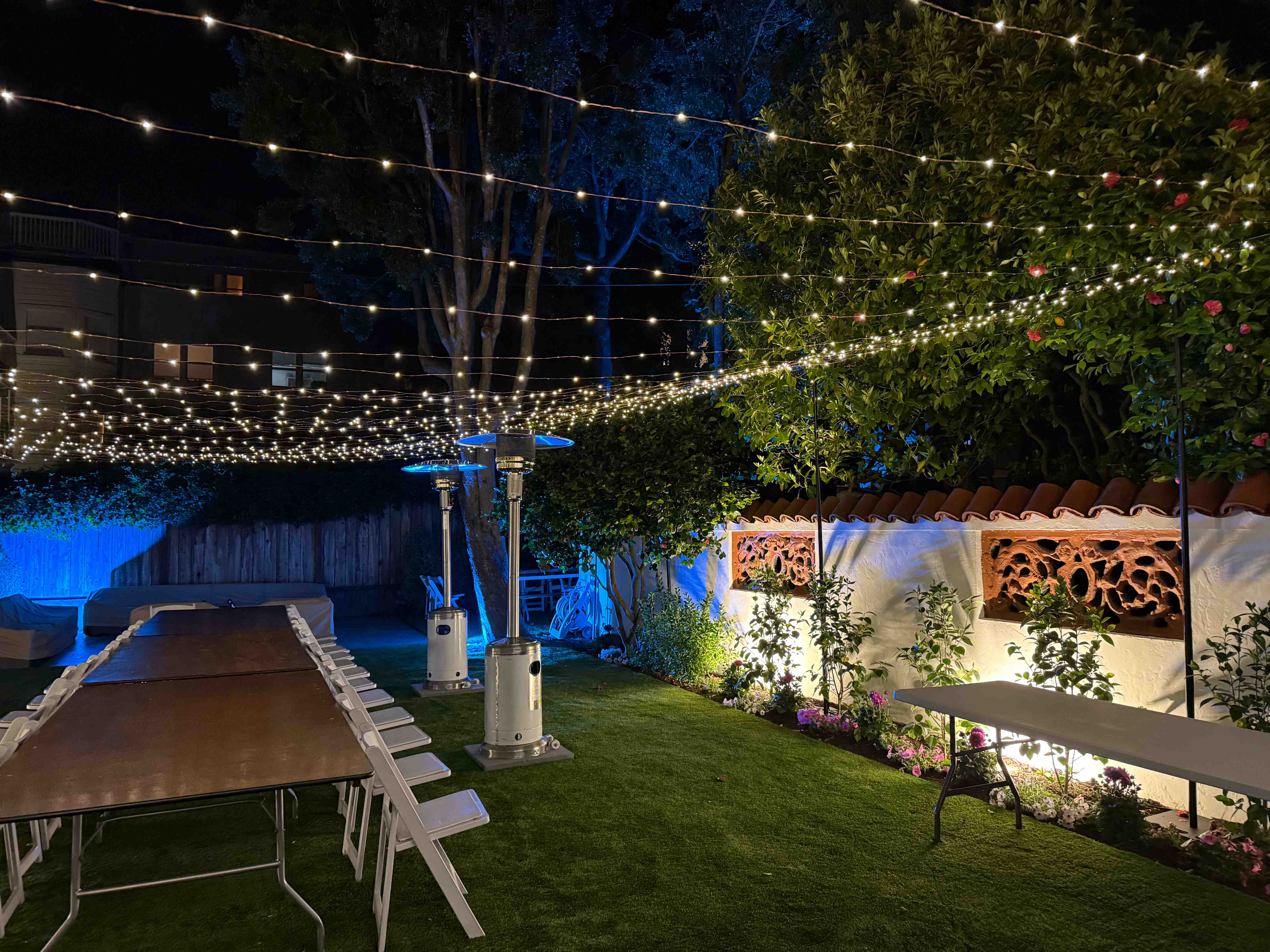 Elegant outdoor dining space with canopy of string lights and accent wall lighting